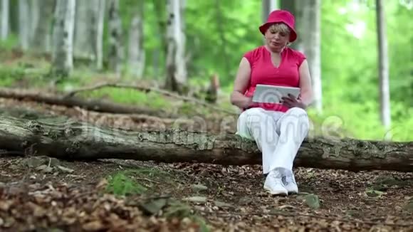 女人坐在森林中一棵倒下的树上使用平板电脑视频的预览图