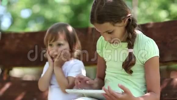 两个姐妹用白色平板电脑坐在秋千凳上视频的预览图