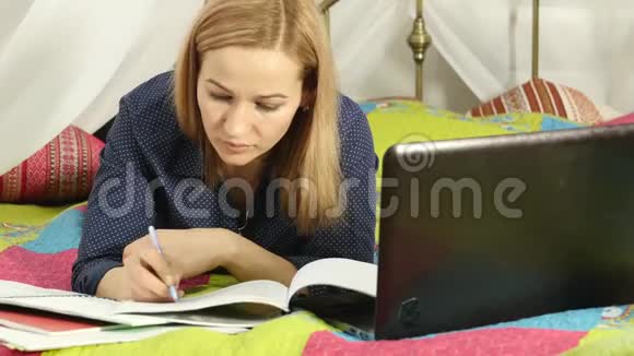 学生躺在家里的床上在笔记本电脑上工作的女人网上教育视频的预览图