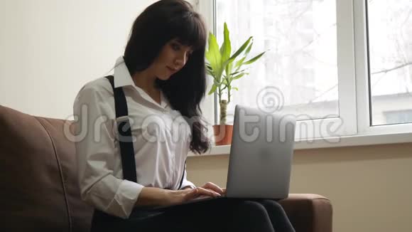 坐在沙发上用笔记本电脑的年轻女子视频的预览图