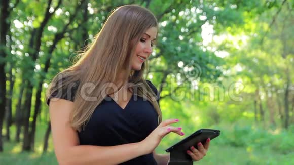 平板电脑上公园里美丽的年轻女子视频的预览图