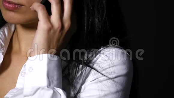 年轻优雅的女人在黑色背景下用手机说话视频的预览图