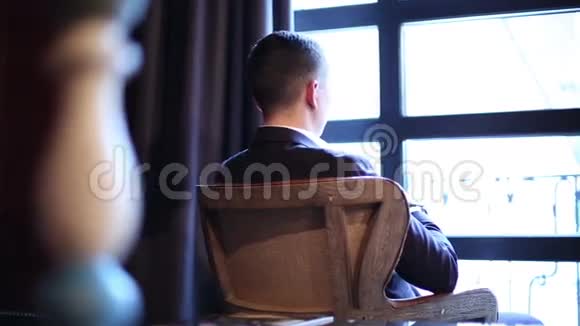 一个体贴的年轻人坐在窗前的复古扶手椅上视频的预览图