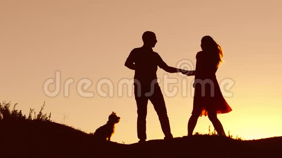 一对相爱的情侣在日落时跳舞剪影和接吻爱的男人和女人与狗跳舞剪影自然慢视频的预览图