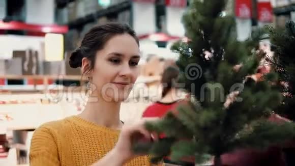 年轻迷人的黑发女孩在商店里选择了一棵人造圣诞树圣诞装饰视频的预览图