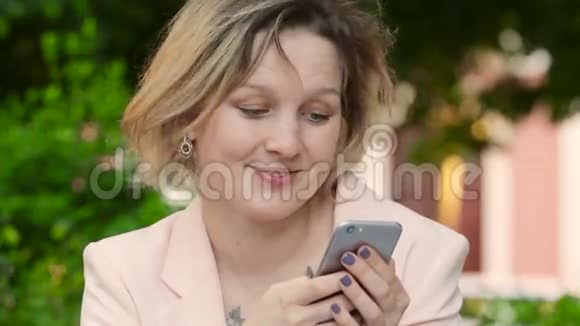 漂亮的金发白女在阳光明媚的日子在公园里自由工作使用智能手机视频的预览图