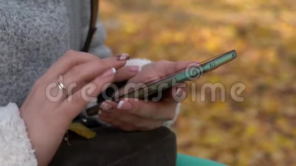 女孩在公园里的智能手机上发短信和打字公园里晴朗的秋日视频的预览图