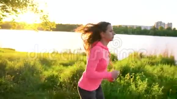 日落时分女人穿过湖岸上的公园慢动作视频的预览图