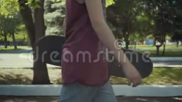 滑板手拿着滑板在公园里散步视频的预览图