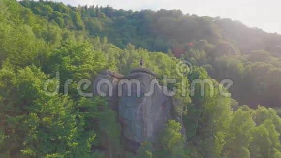 英俊的年轻运动员赤裸的躯干摆在绿林山环绕的岩石上视频的预览图