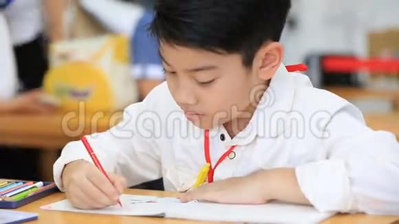 快乐的亚洲男孩在教室的笔记本上写字视频的预览图