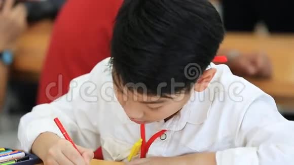 快乐的亚洲男孩在教室的笔记本上写字视频的预览图