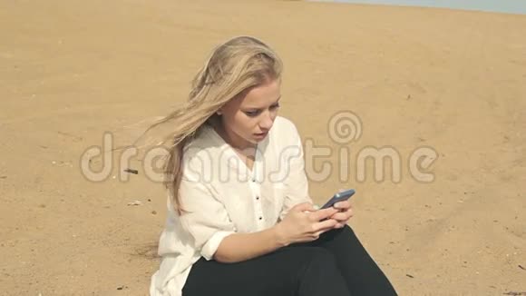 美丽的女孩坐在沙滩上打电话视频的预览图