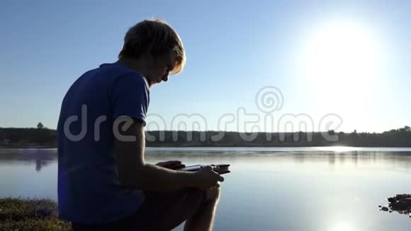 一个年轻人夏天在湖岸看一张家庭相册视频的预览图