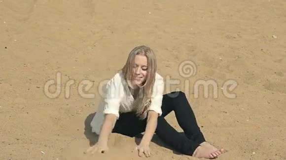 美丽的女孩坐在沙滩上看着视频的预览图
