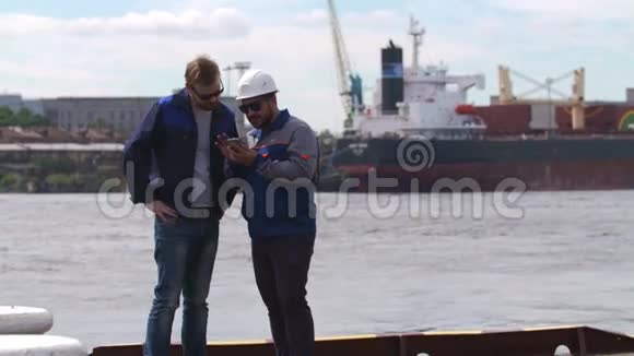 两个好朋友码头工人和同事在航运货运港看智能手机视频的预览图