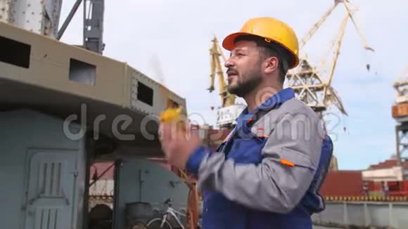 带黄色头盔和对讲机的码头工人指挥装运港的货物起重机视频的预览图