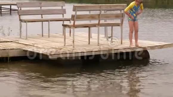 穿着泳衣的有趣的孩子坐在河边的木桥上摆动他们的腿创造喷雾男孩在度假时很开心视频的预览图