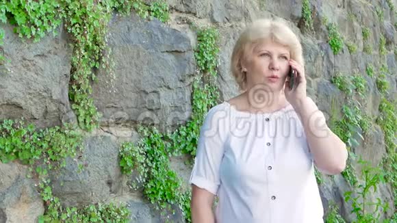 使用智能手机的老年妇女背景中野生石头的复古墙视频的预览图