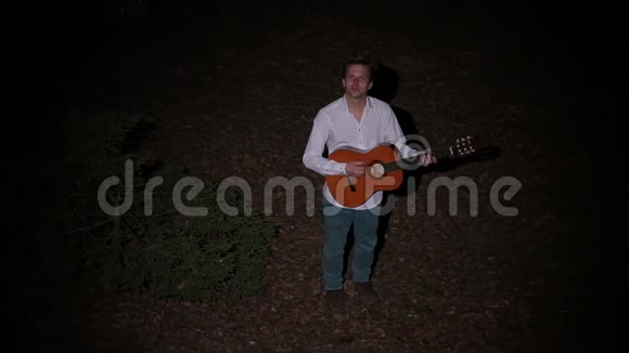 一个穿着白色衬衫的可爱的年轻人弹吉他唱小夜曲视频的预览图