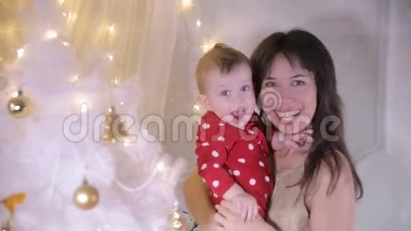 小宝宝和他妈妈在圣诞树附近玩耍新年装饰和第一步的概念视频的预览图