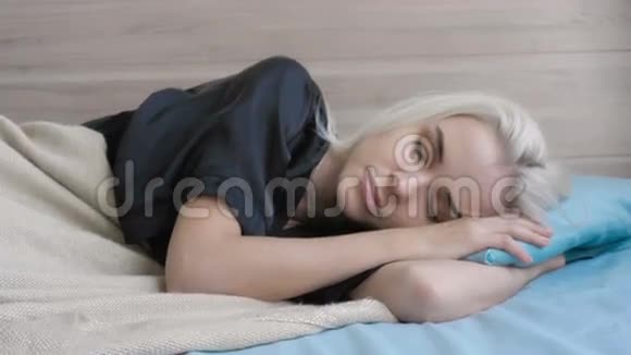 美丽的金发女郎在家中醒来并躺在床上视频的预览图