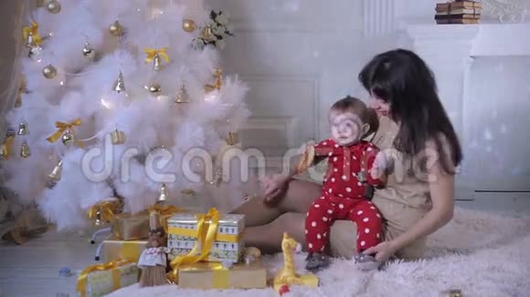 小宝宝和他妈妈在圣诞树附近玩耍新年装饰和第一步的概念视频的预览图