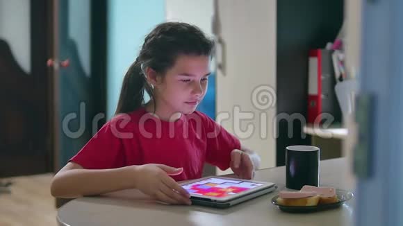 少女正在吃三明治在平板电脑上玩一个网络游戏女童社交媒体室内平板电脑视频的预览图