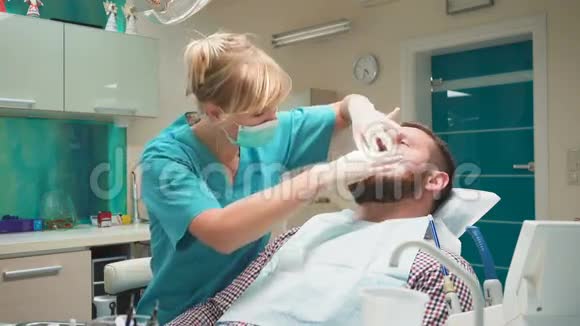 女牙医检查男性病人的牙齿看着相机视频的预览图