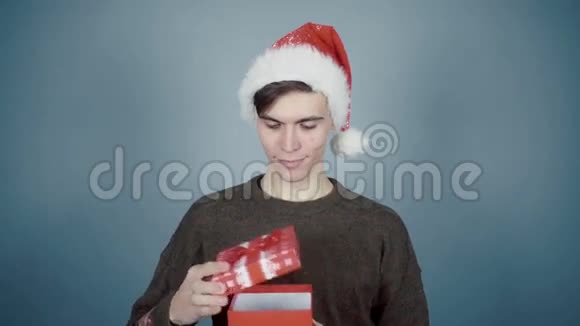 戴着圣诞帽的年轻人打开了一个礼品盒里面有一个惊喜看到了小红色的包裹视频的预览图