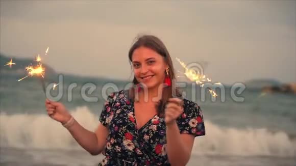 年轻快乐的微笑女人在日落时与火花在缓慢的运动中跳舞在海滩上的日落时与烟花一起跳舞视频的预览图