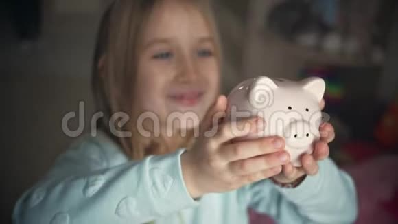 快乐的女孩把钱存到家里的储蓄罐里孩子将硬币插入储蓄罐室内金融概念孩子视频的预览图