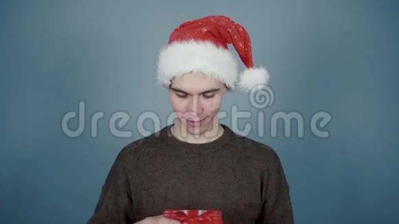 戴着圣诞帽的年轻人打开礼物盒看到里面有电话智能手机视频的预览图