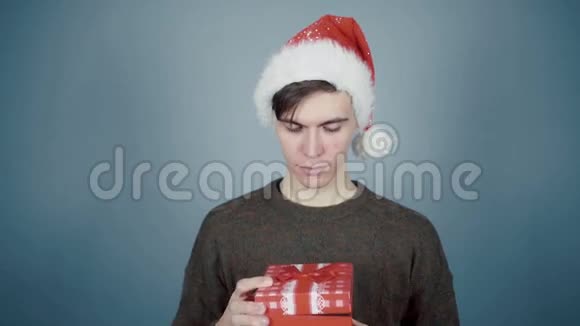 戴着圣诞帽的年轻人打开一个礼品盒里面有一个惊喜看到燃烧的蜡烛视频的预览图