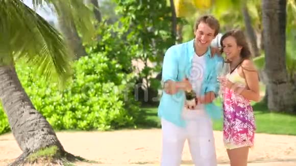 年轻的幸福夫妇在海滩上开着瓶香槟视频的预览图