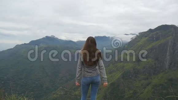 小女孩伸出山顶举起双手站在美丽峡谷边缘的女游客视频的预览图