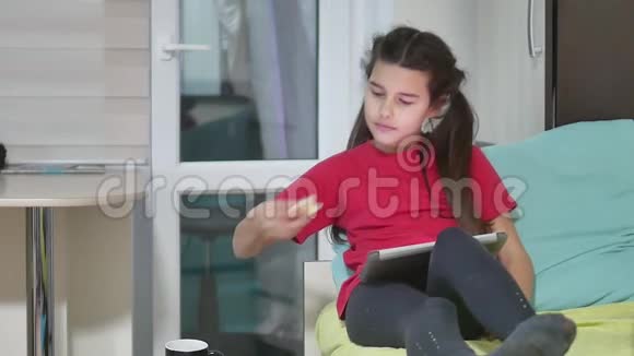 少女正在吃三明治在平板电脑上玩一个网络游戏女童社交媒体室内互联网视频的预览图