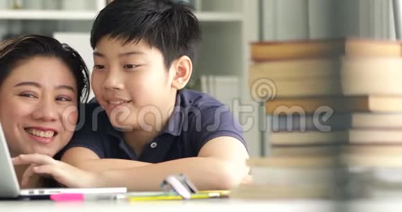 可爱的亚洲妈妈帮助你的儿子在家里做作业微笑着一起视频的预览图