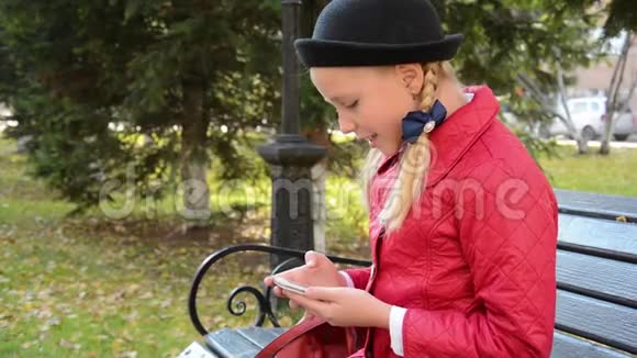 今年秋天城市公园的一位年轻女孩在智能手机上使用应用程序坐在长椅上视频的预览图