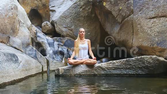 水中石上上莲花瑜伽中的金发女郎视频的预览图