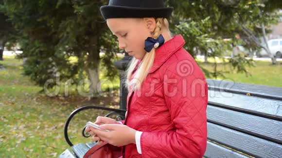 今年秋天城市公园的一位年轻女孩在智能手机上使用应用程序坐在长椅上视频的预览图