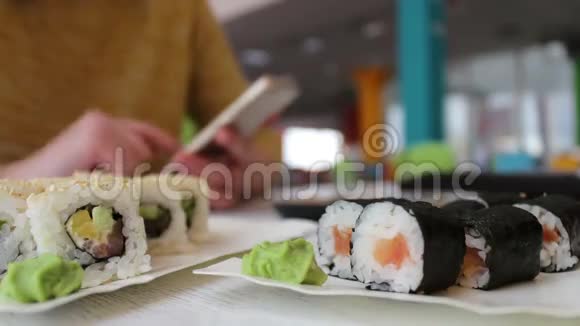 女孩坐在智能手机上打字与桌上咖啡馆里的对话者交流的是寿司日本菜视频的预览图