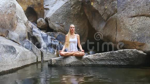 水中石上上莲花瑜伽中的金发女郎视频的预览图