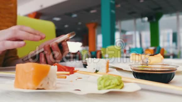 女孩坐在智能手机上打字与桌上咖啡馆里的对话者交流的是寿司日本菜视频的预览图