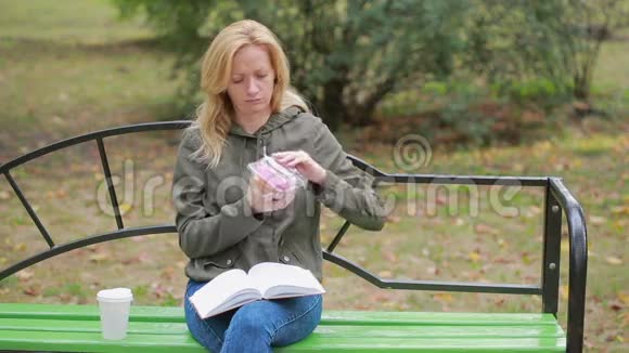 公园里的金发女孩吃甜甜圈户外女人吃甜面包视频的预览图
