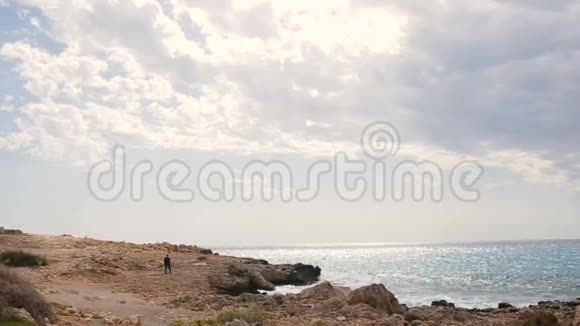 在一个美丽的阳光明媚的日子里男人在岩石海滩边散步塞浦路斯视频的预览图