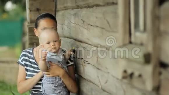 漂亮的小男孩坐在妈妈的手上吃黄瓜在老木屋附近视频的预览图