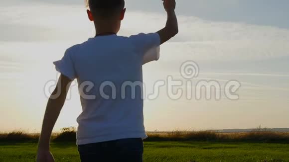 快乐的家伙在阳光下的田野里玩纸飞机日落时剪影视频的预览图