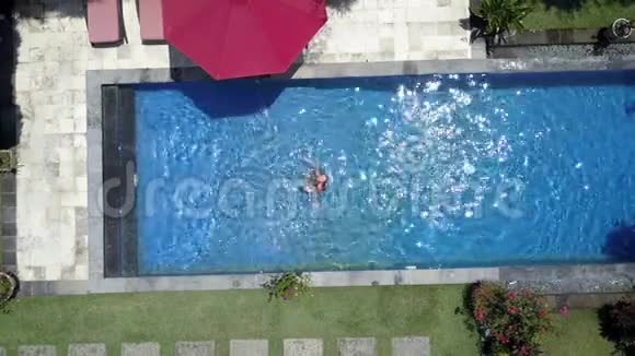 这位年轻的美女在一个热带花园的游泳池里游泳从无人机上可以看到空中景色视频的预览图
