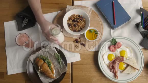 咖啡厅健康早餐的顶级景观人在格兰诺拉浇牛奶英式早餐煎鸡蛋培根吐司在盘子里视频的预览图